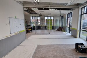 Open office during renovation with metal scaffolding, broken ceiling tiles, and exposed ductwork area center-right.